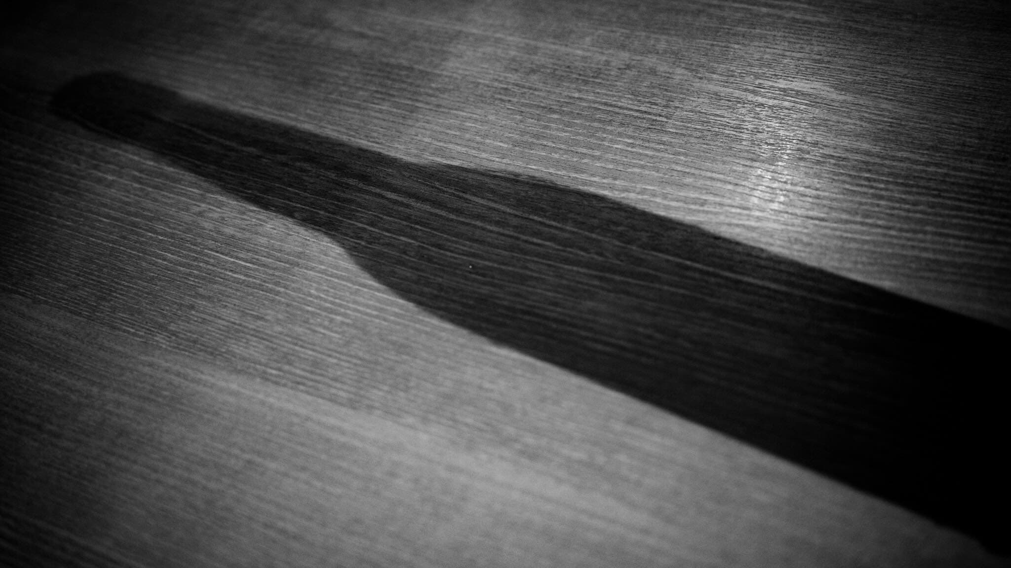 木目の走る板の上に、斜めに伸びる濃い影が落ちているモノクロの接写