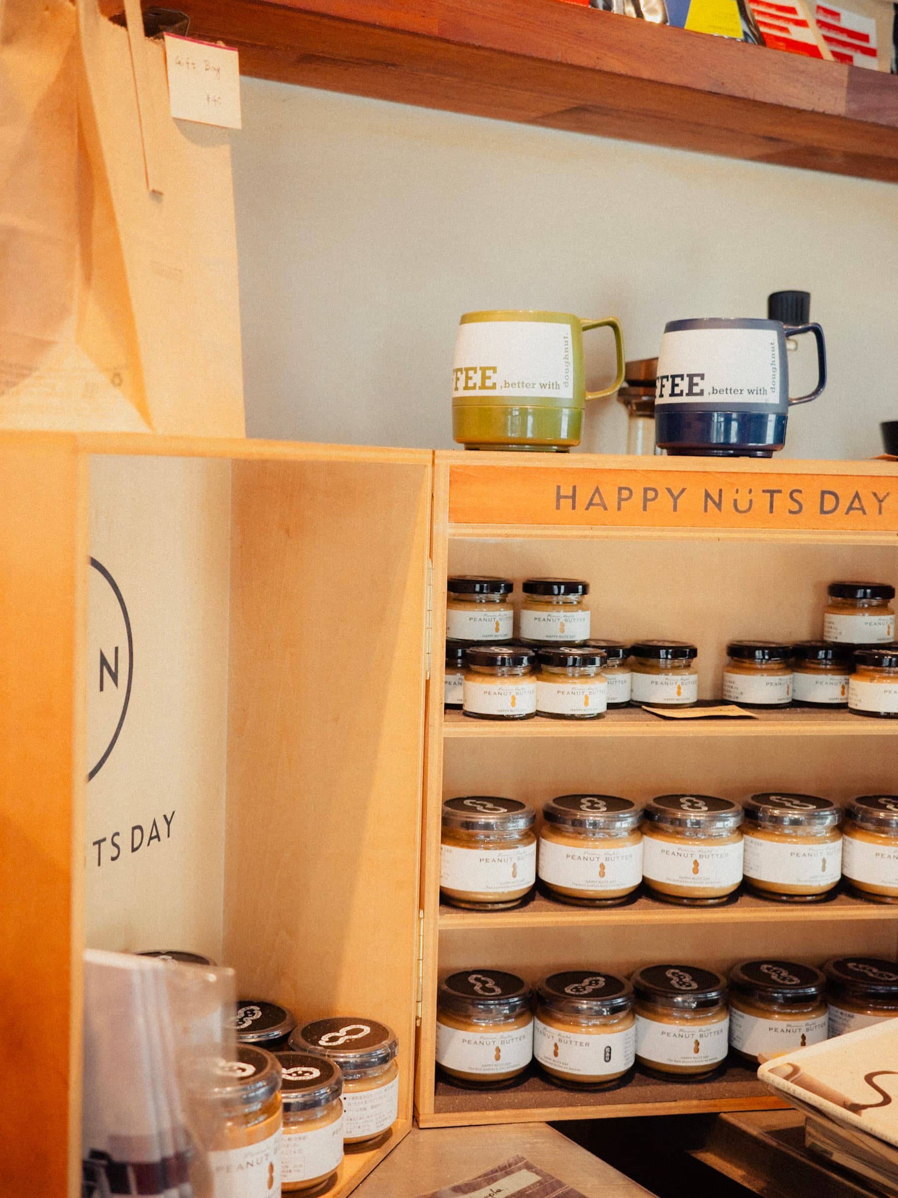 木箱の棚に並ぶHAPPY NUTS DAYのピーナッツバターの瓶。上の棚にはCOFFEEと書かれた緑と紺のマグカップが2つ置かれている